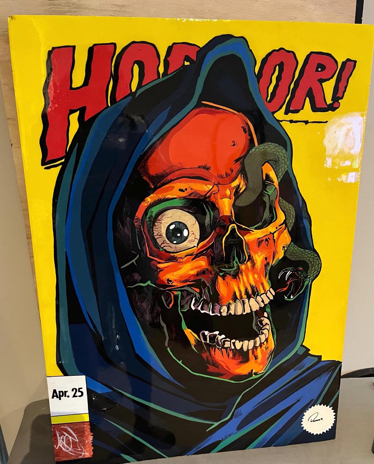 Skeleton Man Wall Art — a large painted panel of an orange skull in a blue hood, leaning against a wall.